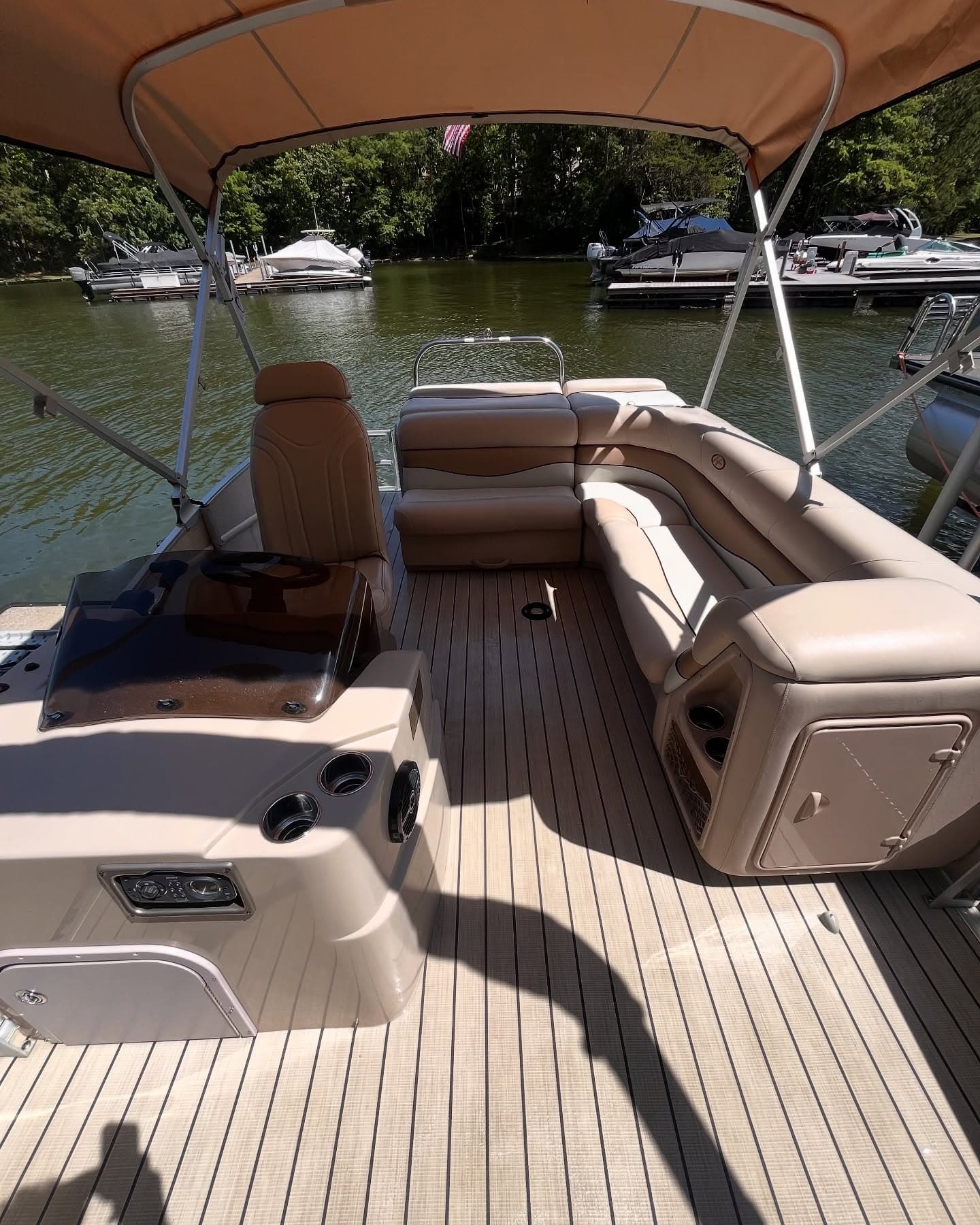 Tan-upholstered pontoon boat deck with bimini top and helm, docked at a Lake Lanier marina