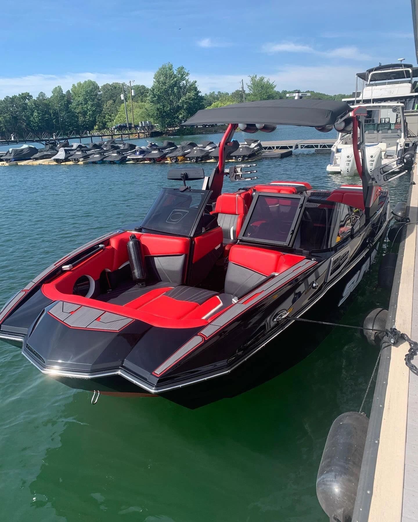 Freshly detailed black and red Supra wake boat, bow view, docked at a Lake Lanier marina