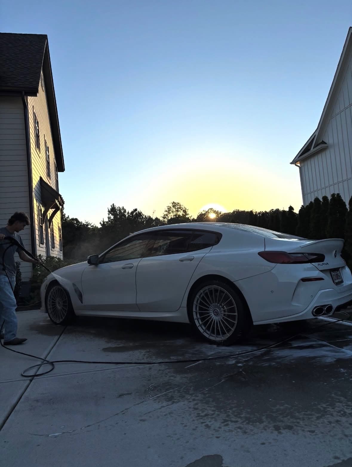Peyton Adams pressure-washing a white BMW Alpina at sunset in a Cumming, GA driveway